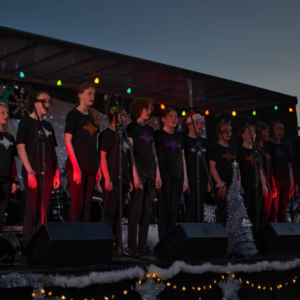 Choir singing at Christmas event outdoors at dusk.