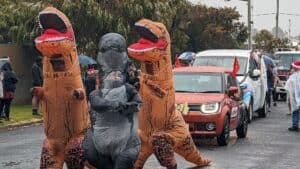 People in dinosaur costumes at festive street parade.