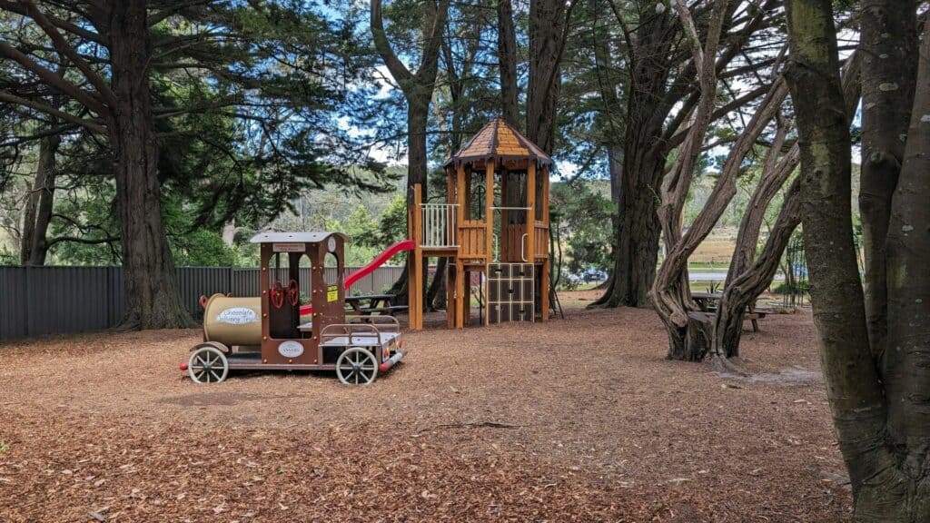 Wooden playground in park with trees and slide.
