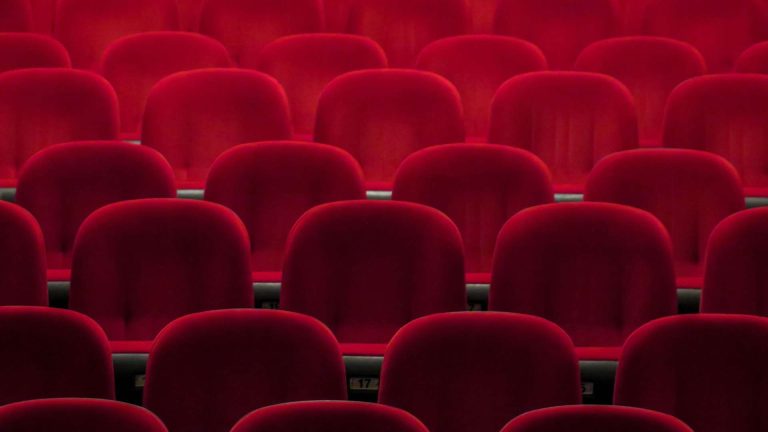 Empty red cinema seats in dim lighting.