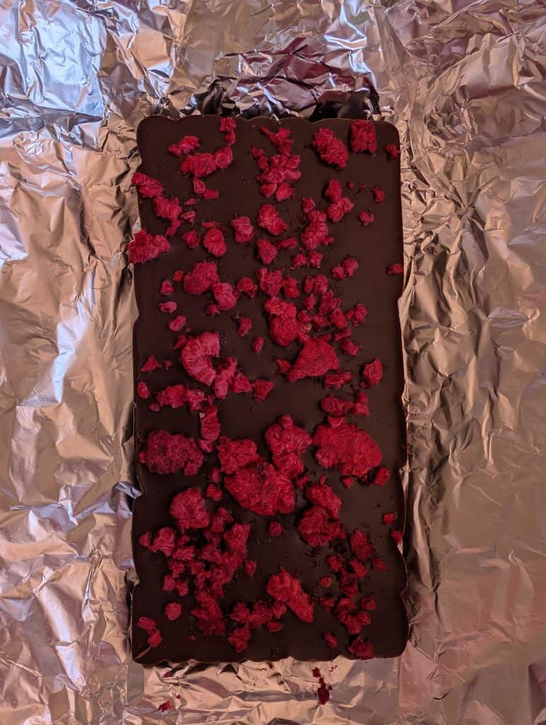 Chocolate bar with freeze-dried raspberries on foil.